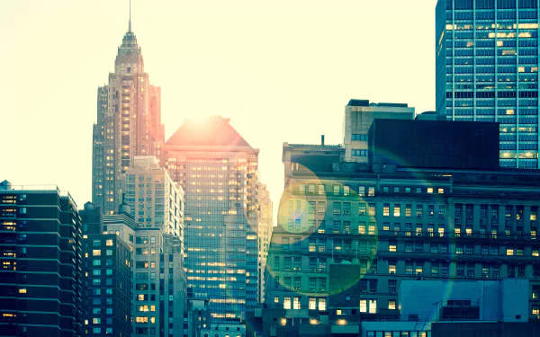 8K Ultra HD PC desktop wallpaper of a sunny New York city skyline, man-made skyscrapers and buildings bathed in warm light with lens flare.