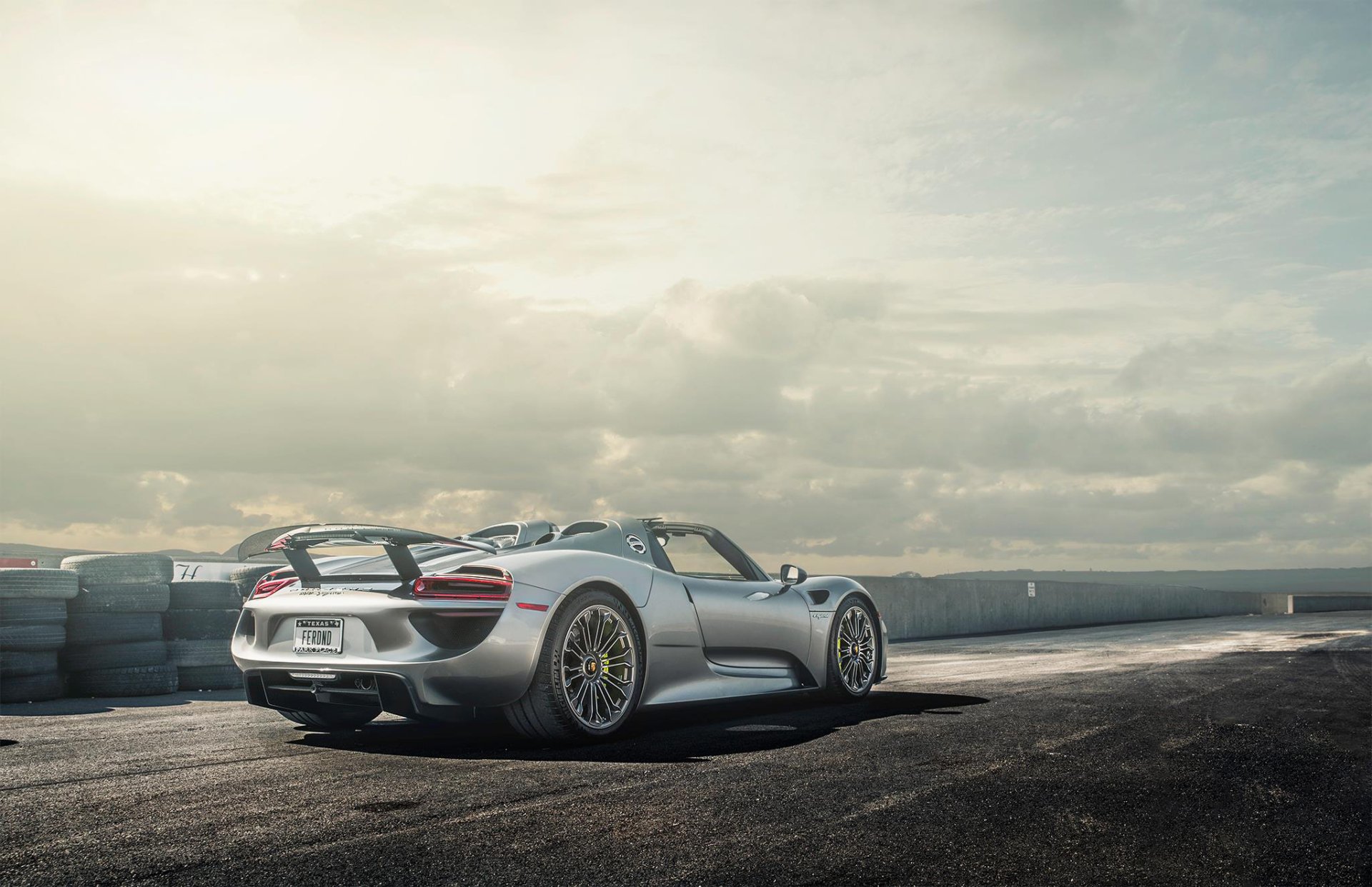 Silver Porsche 918 Spyder supercar parked on a racetrack under a cloudy sky, captured in HD for a sleek PC desktop wallpaper background.