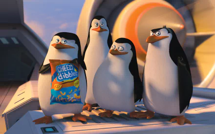 HD PC desktop wallpaper featuring the four penguin characters from the movie Penguins of Madagascar standing together with a box of Cheezy Nibbles.