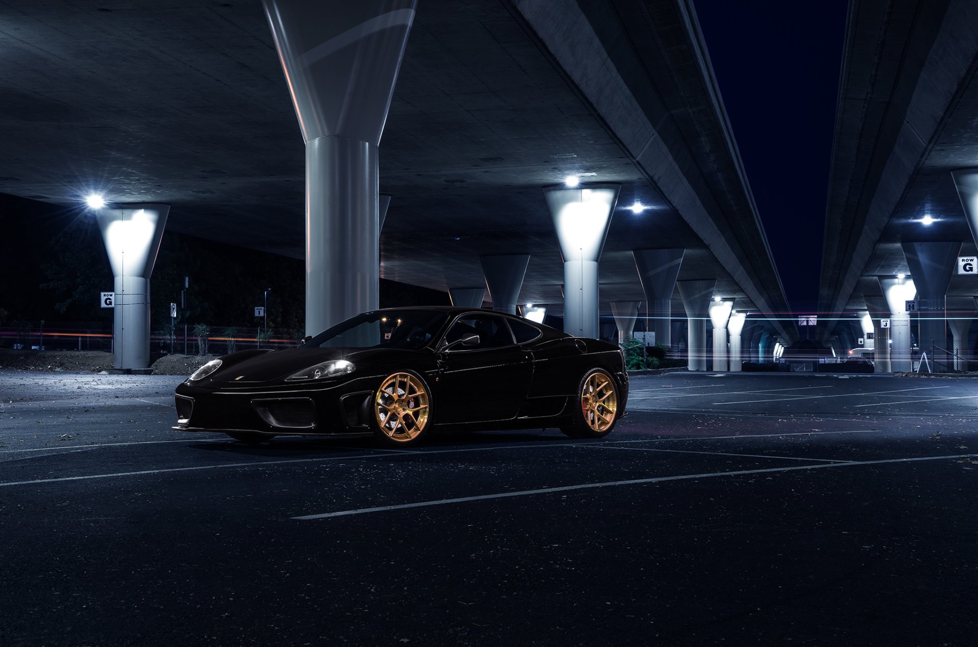 Black Ferrari 360 Modena supercar with gold rims parked under an urban bridge at night, showcased as an HD PC desktop wallpaper and background.
