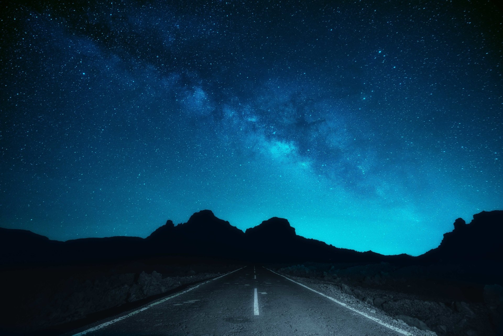 A serene night road stretches into the distance, illuminated under a stunning Milky Way backdrop, creating a captivating sci-fi atmosphere in this 4K Ultra HD wallpaper.