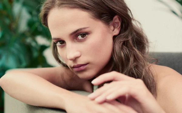 A close-up of Alicia Vikander, a Swedish actress with brown eyes and brunette hair, set against a bokeh background, creating an elegant HD desktop wallpaper.