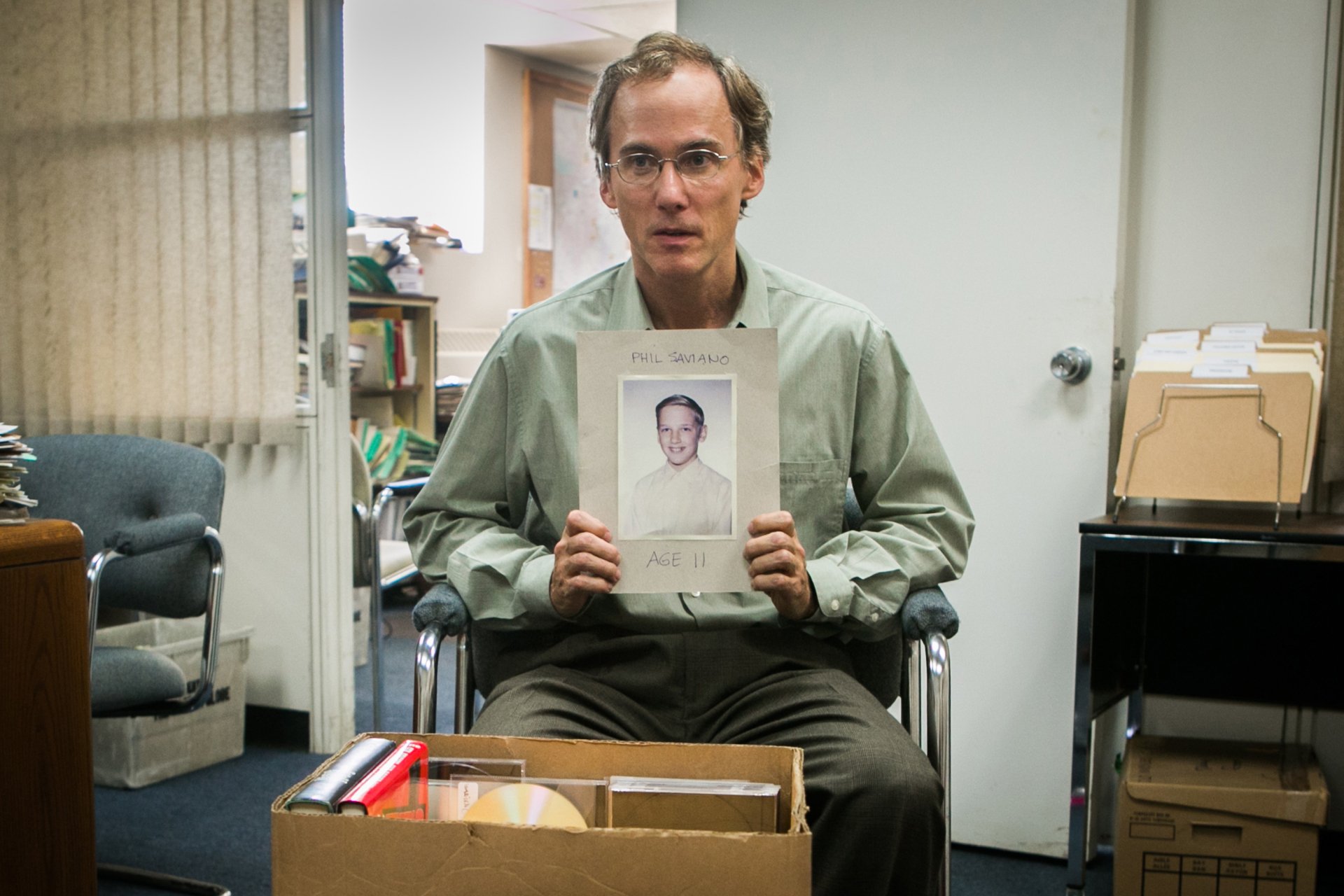 2K Quad HD PC desktop wallpaper: scene from the movie Spotlight (2015) — a man in an office holds a portrait amid boxes and files.