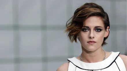 HD desktop wallpaper featuring actress Kristen Stewart with green eyes and brunette hair against a blurred gray background.