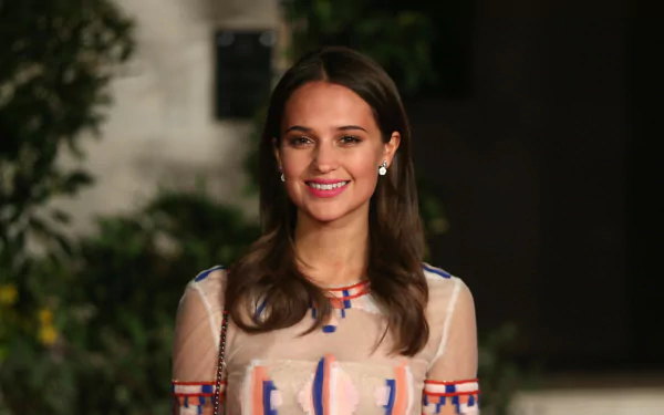 HD desktop wallpaper of Swedish actress Alicia Vikander with brunette hair, brown eyes, and a warm smile against a softly blurred background.