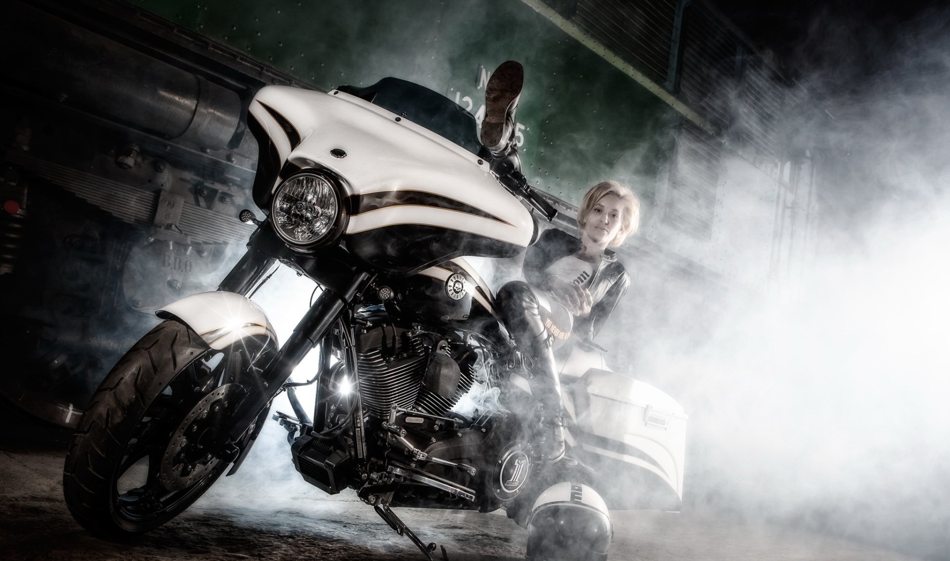 HD PC desktop wallpaper: woman in biker gear poses on a chrome motorcycle amid smoke and dramatic lighting — Girls & Motorcycles background with close-up bike detail.