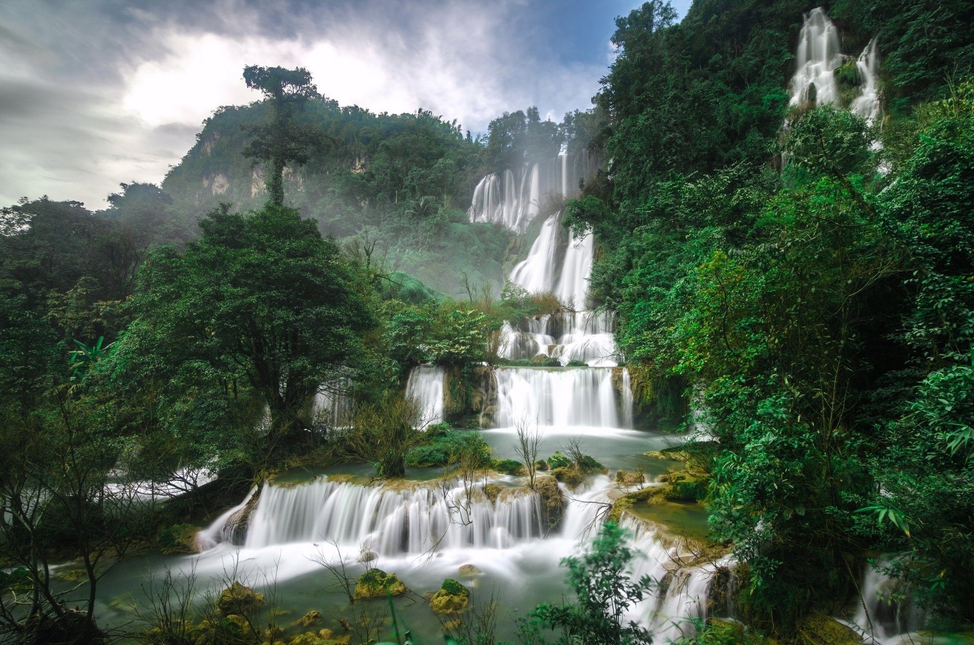 A stunning waterfall cascades through lush greenery in a vibrant Thai rainforest, showcasing the natural beauty of Thailand's diverse landscape.