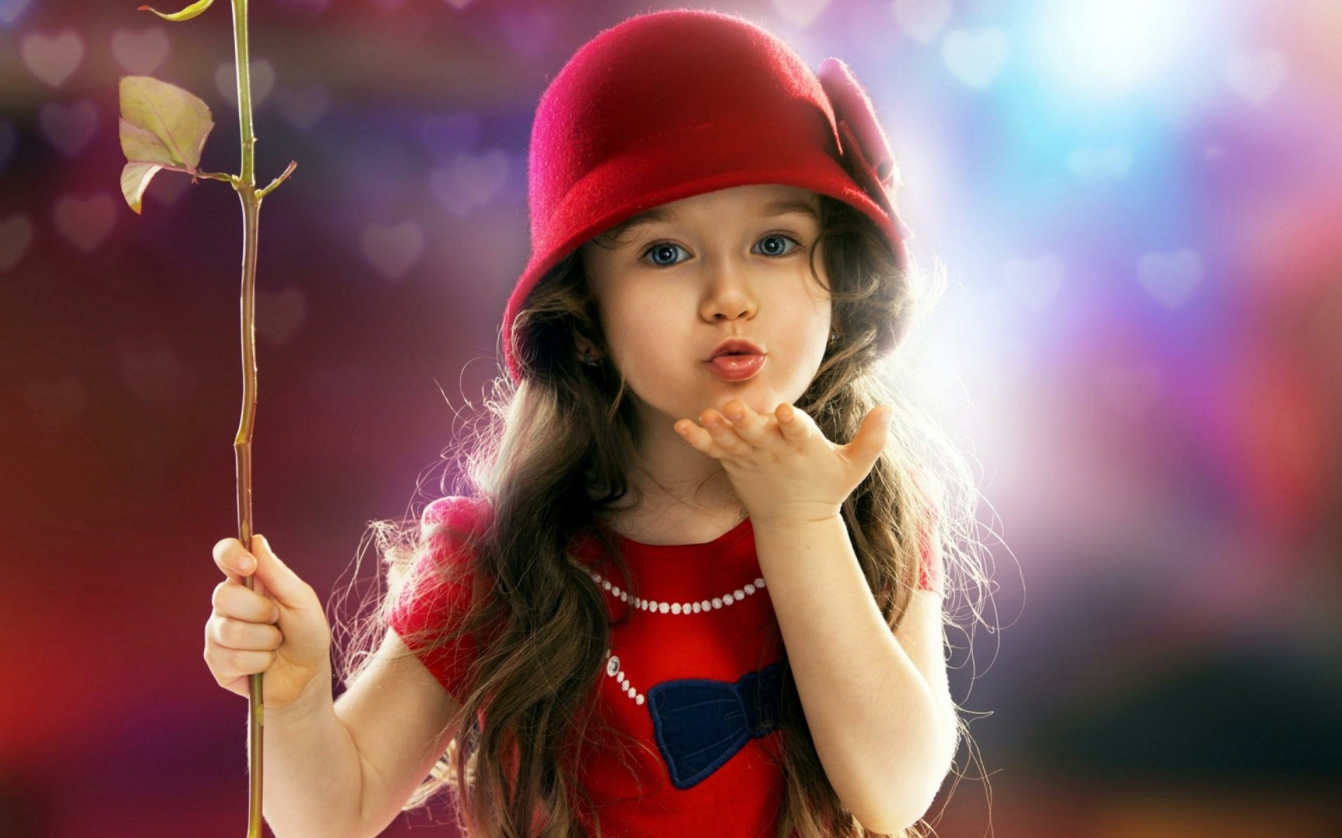 HD wallpaper featuring a cute little girl in a red hat, blowing a kiss while holding a stick. The colorful, dreamy background enhances the photography's charm.