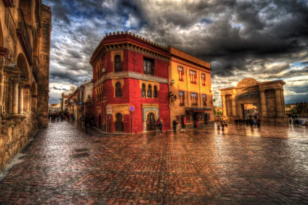 HDR photograph of a historic square in Córdoba, Spain, featuring vibrant architecture and wet cobblestone streets under a dramatic cloudy sky.