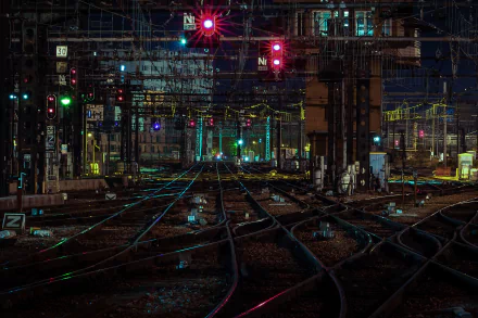 A vibrant night scene of a man-made railroad yard illuminated by colorful lights and signals, showcasing intricate tracks converging in a captivating, high-definition wallpaper.