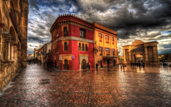 HDR photograph of a historic square in Córdoba, Spain, featuring vibrant architecture and wet cobblestone streets under a dramatic cloudy sky.