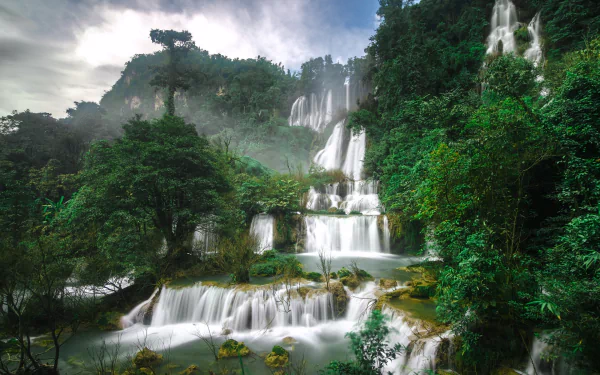 A stunning waterfall cascades through lush greenery in a vibrant Thai rainforest, showcasing the natural beauty of Thailand's diverse landscape.