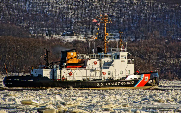 A U.S. Coast Guard boat navigates through icy waters of the Hudson River, surrounded by a winter landscape, captured in stunning HD detail.