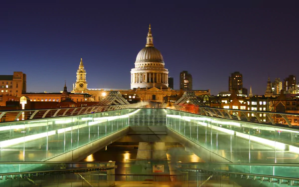 Night view of St Paul's Cathedral and Millennium Bridge illuminated against the London cityscape, showcasing the iconic religious monument and surrounding buildings in the United Kingdom.