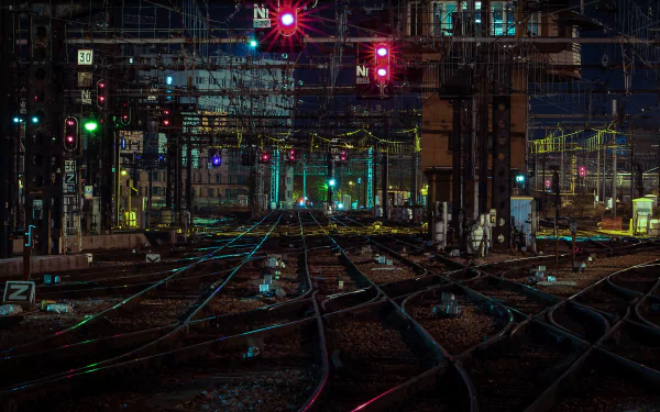A vibrant night scene of a man-made railroad yard illuminated by colorful lights and signals, showcasing intricate tracks converging in a captivating, high-definition wallpaper.