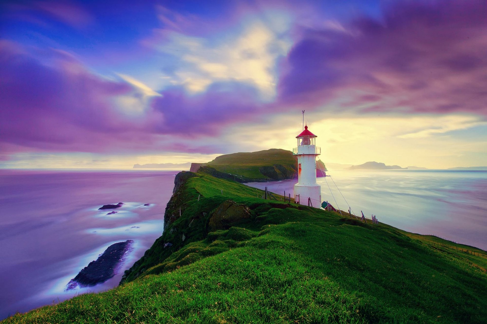 Lighthouse perched on a cliff overlooking the ocean at purple-hued horizon under dramatic clouds in the Faroe Islands, captured in HD for desktop wallpaper.