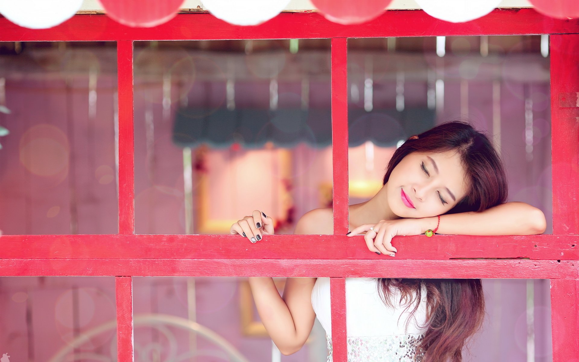 A brunette Asian woman with lipstick leans against a red window frame, eyes closed in a peaceful mood. This high-definition wallpaper captures a serene and contemplative moment.