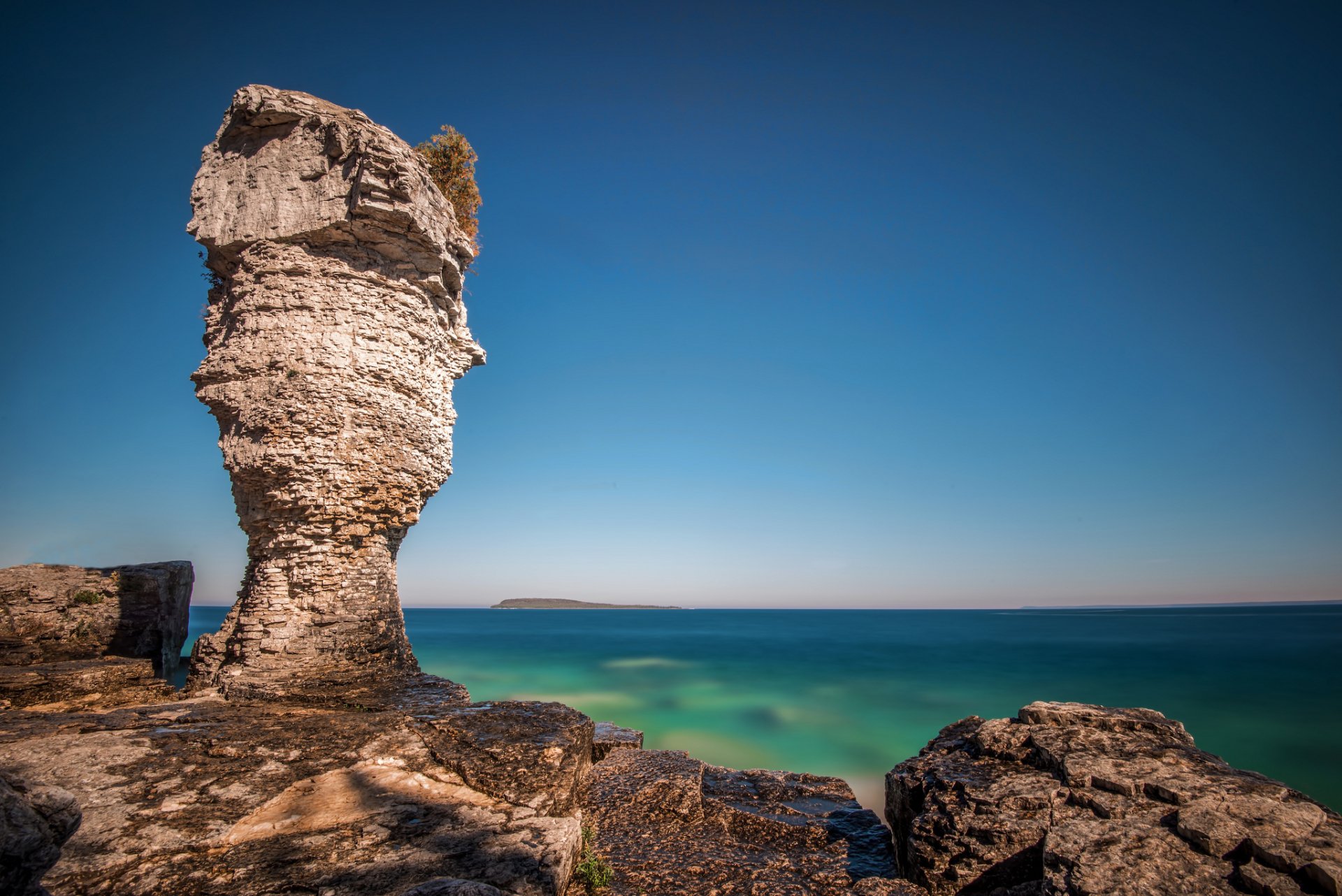 HD desktop wallpaper showing a striking limestone rock formation by the ocean horizon in Ontario, with clear blue skies and calm waters in a natural coastal landscape.