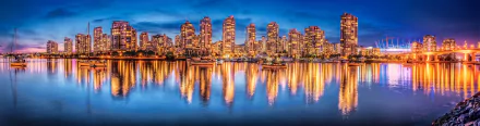 Panoramic night view of Vancouver's illuminated skyscrapers reflecting on calm water, showcasing the cityscape of British Columbia, Canada.