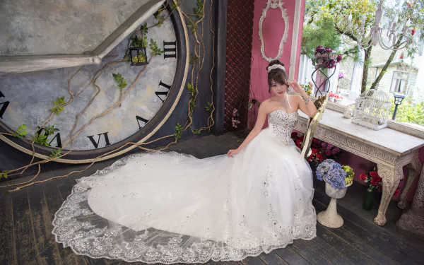 An oriental bride in a white wedding dress poses elegantly beside a large vintage clock, set against a charming, rustic interior. Suitable as an HD desktop wallpaper.