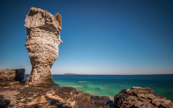 HD desktop wallpaper showing a striking limestone rock formation by the ocean horizon in Ontario, with clear blue skies and calm waters in a natural coastal landscape.