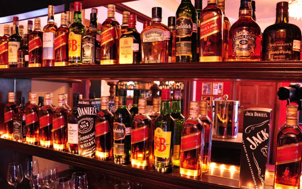 A vibrant shelf showcasing an array of whiskey bottles, including Chivas Regal and Jack Daniel's, illuminated with soft lighting, creating an inviting atmosphere for whisky enthusiasts.