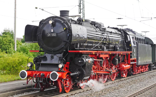 A detailed HD desktop wallpaper of a black and red steam locomotive train on railway tracks with green foliage in the background.