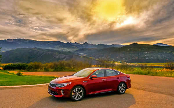 A red Kia Optima car parked on a scenic road with mountains and a dramatic sunset sky in the background, captured in 4K Ultra HD quality.