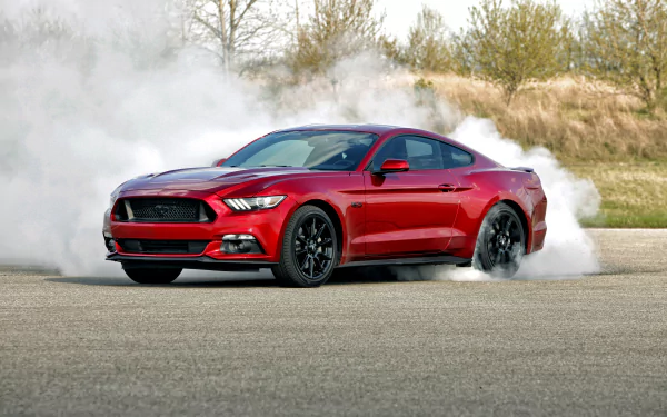 A vibrant red Ford Mustang GT muscle car kicks up smoke during a dynamic display on an open road, showcasing its powerful design and performance. HD wallpaper backdrop for car enthusiasts.