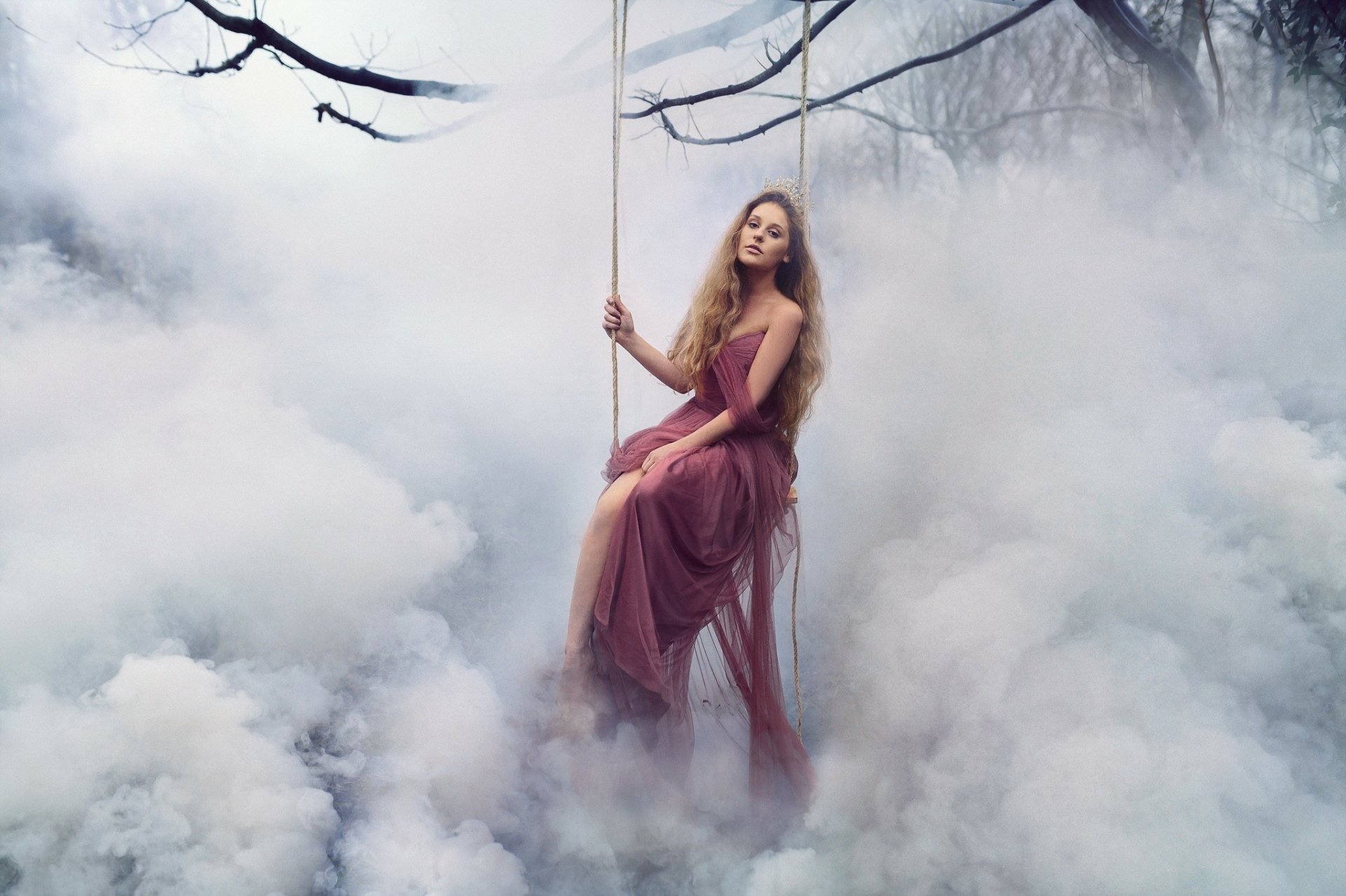 A blonde woman wearing a crown sits gracefully on a swing surrounded by thick fog and clouds in a fantasy-themed, artistic HD desktop wallpaper.