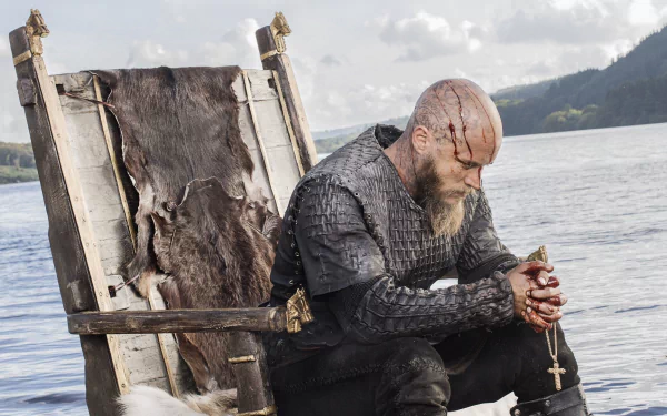 Ragnar Lothbrok sits pensively on a throne by the water in this HD wallpaper from the TV show Vikings (2013), capturing a moment of reflection.