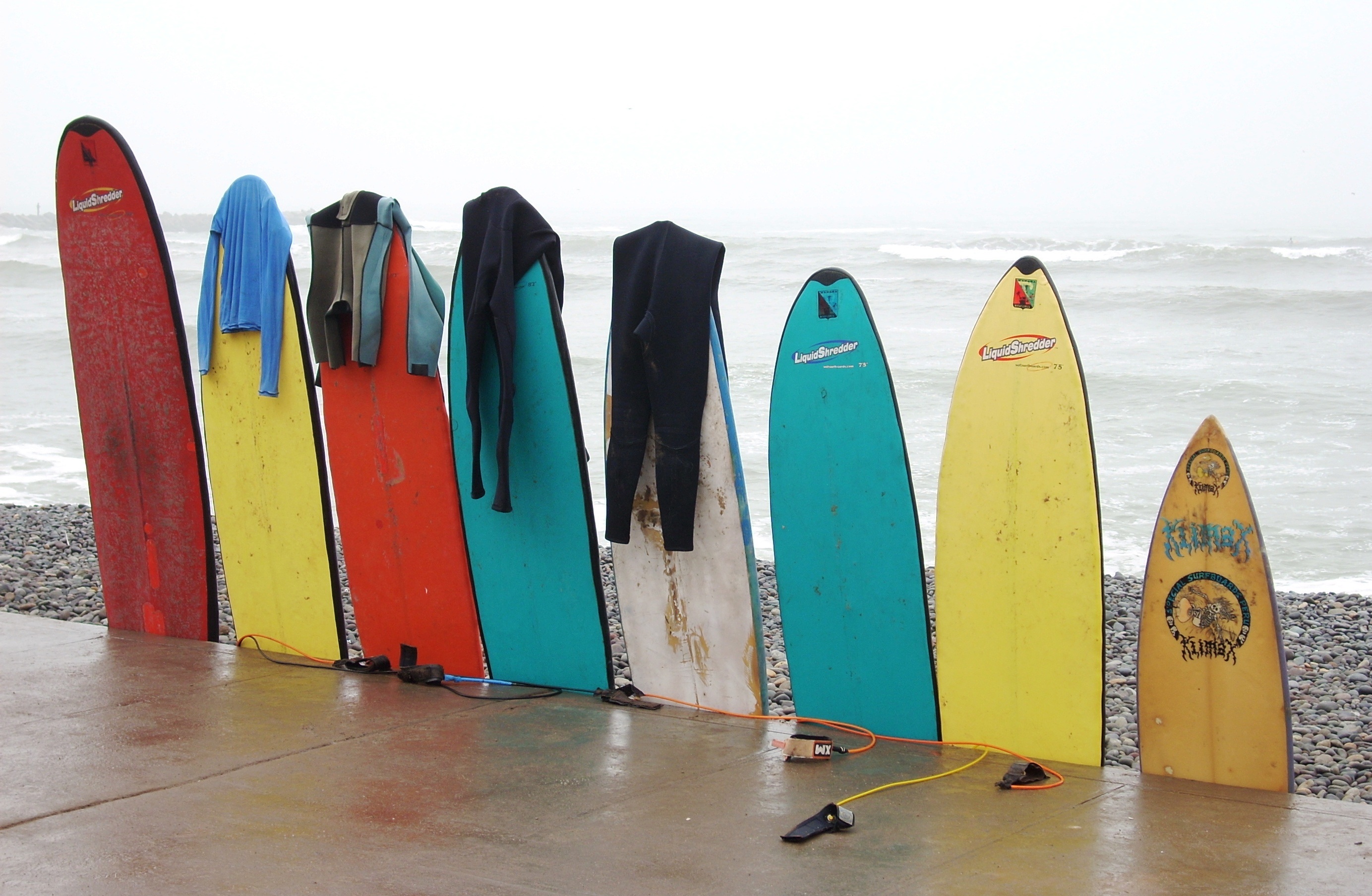 A row of surfboards with wetsuits hanging off them by JPataG
