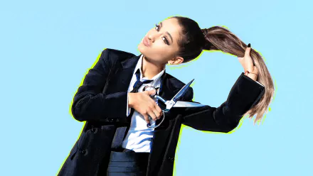 Ariana Grande, a brunette singer in a suit, playfully holds scissors while lifting her ponytail against a bright blue background. Her expressive brown eyes add to the fun vibe.