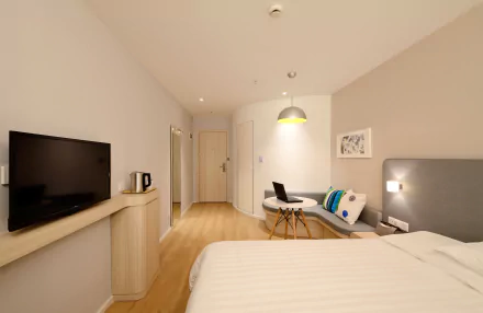 A modern hotel room with a bed, cushioned seating area, table with a laptop, wall-mounted television, and soft lighting in 4K Ultra HD resolution.