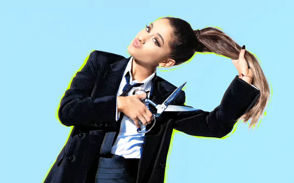 Ariana Grande, a brunette singer in a suit, playfully holds scissors while lifting her ponytail against a bright blue background. Her expressive brown eyes add to the fun vibe.