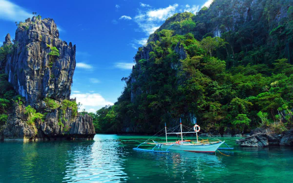 A serene boat floats in the clear waters of Thailand, surrounded by lush green cliffs and a vibrant blue sky, capturing the beauty of the ocean and Earth’s natural wonders.