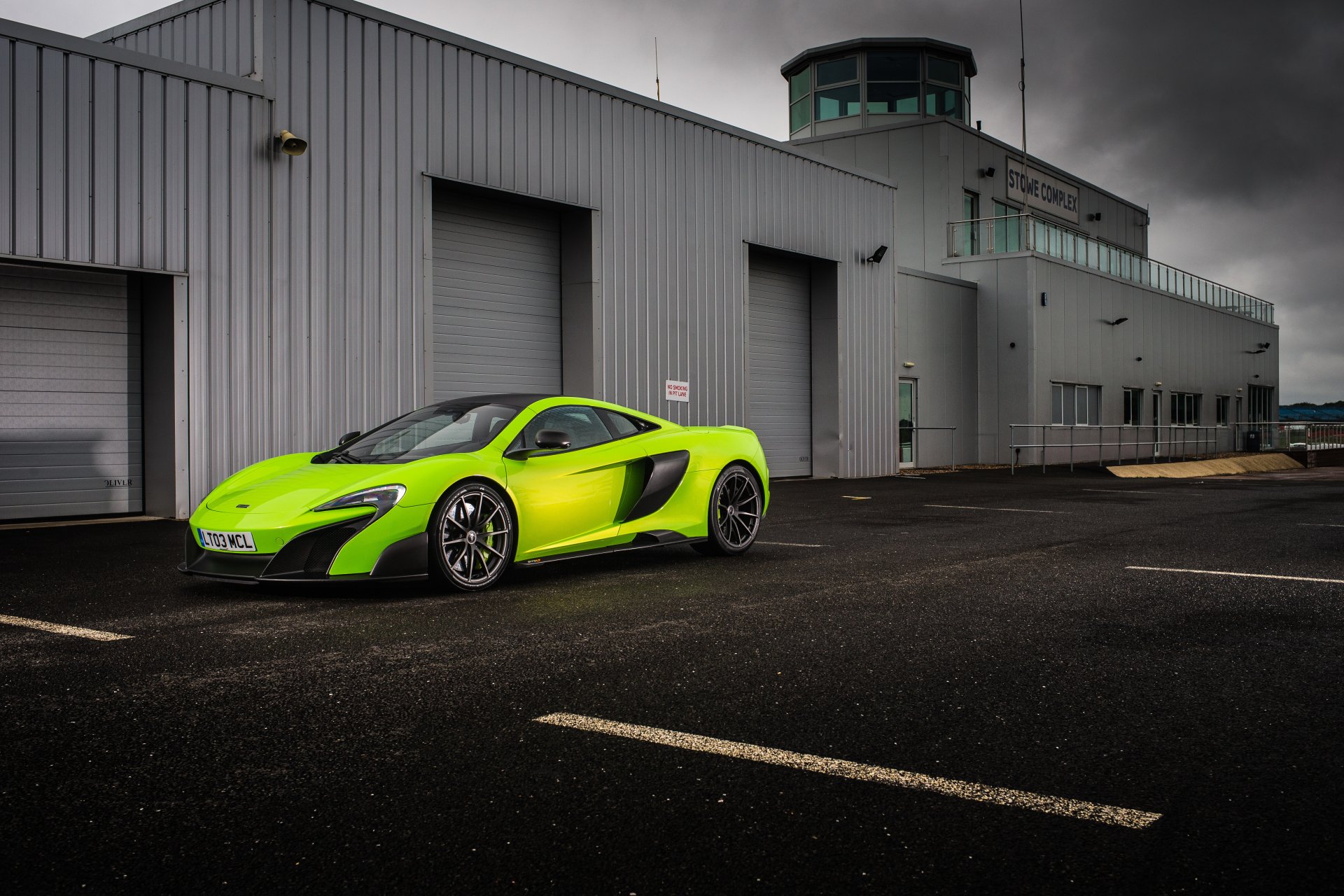 Green McLaren 675LT supercar parked beside an industrial hangar — sleek car and high-performance vehicle rendered as a 5K Ultra HD PC desktop wallpaper/background.