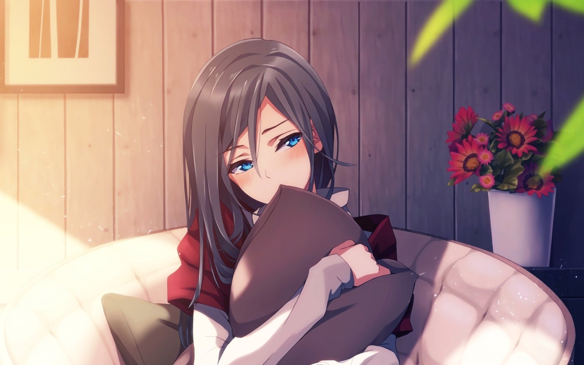 HD desktop wallpaper of an anime girl with long dark hair and blue eyes, sitting on a couch and hugging a pillow. The background features wooden paneling, a framed picture, and a vase with flowers.