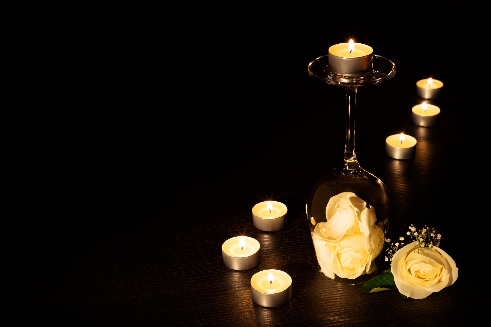 4K Ultra HD still life wallpaper featuring a yellow rose inside an inverted glass surrounded by lit candles casting warm light on a dark surface.