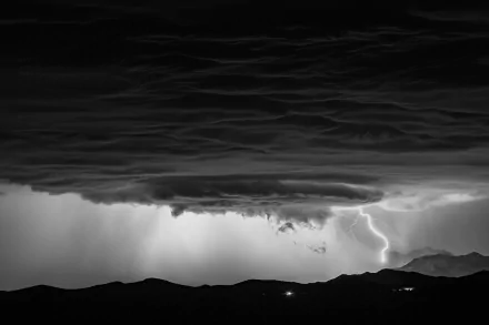A striking black and white image showcasing a storm with dramatic clouds and lightning, creating a powerful connection to nature's awe-inspiring beauty. HD wallpaper for desktop use.