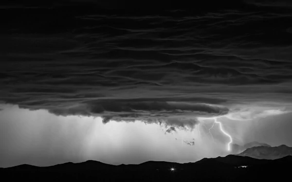A striking black and white image showcasing a storm with dramatic clouds and lightning, creating a powerful connection to nature's awe-inspiring beauty. HD wallpaper for desktop use.