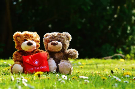Two teddy bear stuffed animals sit on grass, one holding a red heart pillow that says Love You Mom, capturing a loving holiday moment for Mother's Day.