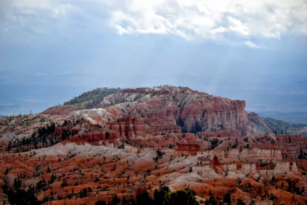 Sunbeams break through clouds over the red rock cliffs and canyon formations of Bryce Canyon National Park, Utah, USA, captured in a stunning HD desktop wallpaper.