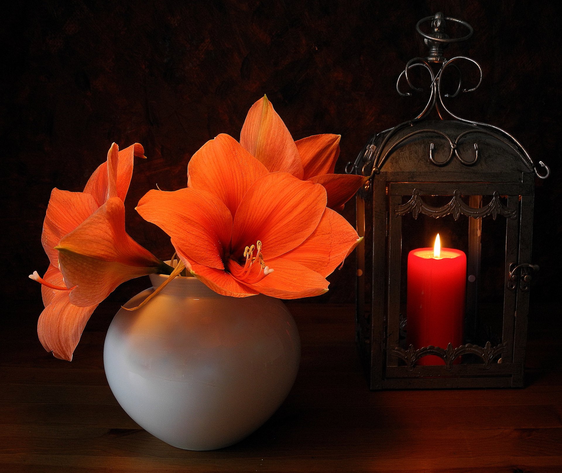 A vibrant orange lily blooms beside a glowing candle in an ornate lantern, all set within a minimalist vase, creating a warm, inviting still life arrangement in this HD desktop wallpaper.