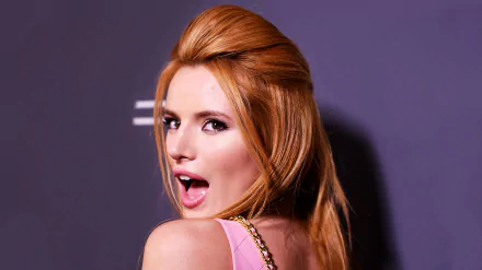 HD desktop wallpaper featuring celebrity Bella Thorne with red hair styled back, wearing a pink outfit against a dark background.