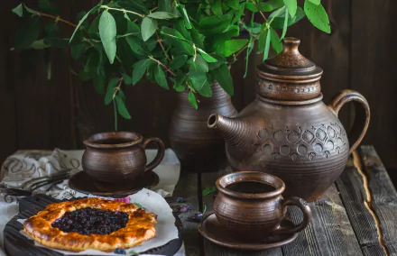 Rustic teapot, kettle, and cups arranged on a wooden table with a pastry and green foliage, captured in an HD PC desktop wallpaper showcasing tea and food.