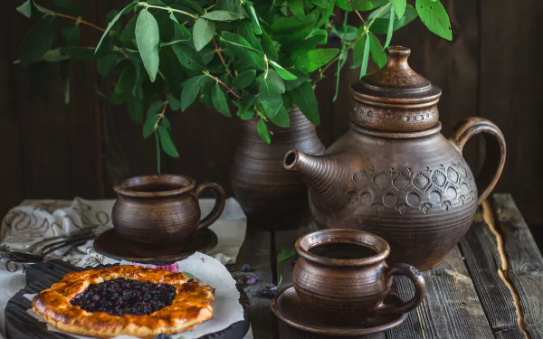 Rustic teapot, kettle, and cups arranged on a wooden table with a pastry and green foliage, captured in an HD PC desktop wallpaper showcasing tea and food.