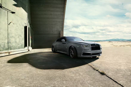 HD desktop wallpaper featuring a sleek Rolls-Royce Wraith parked under a large industrial overhang with a sandy landscape and cloudy sky in the background.