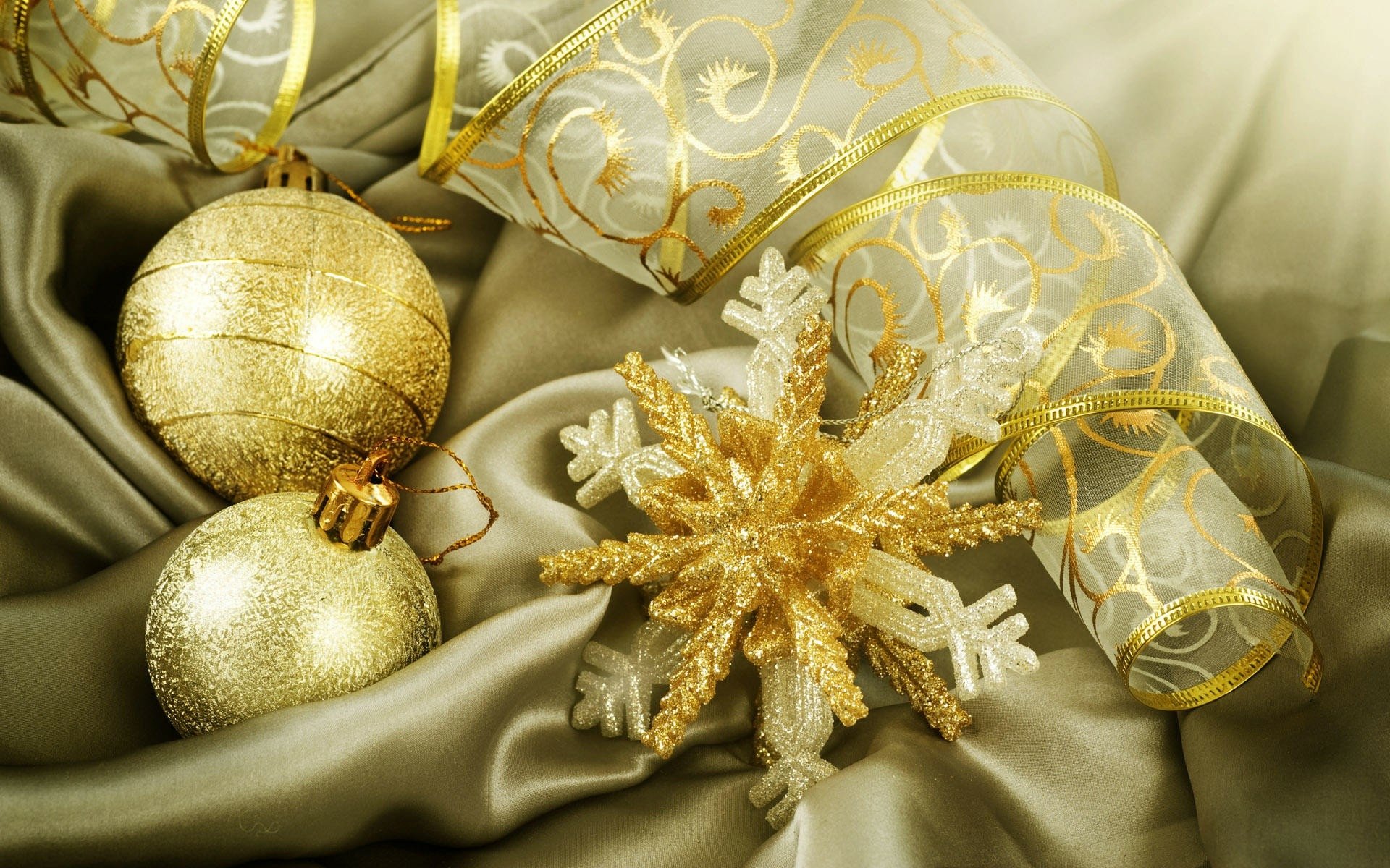 HD desktop wallpaper featuring gold Christmas ornaments and a glittering snowflake on luxurious satin fabric with elegant holiday ribbon accents.