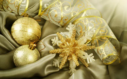HD desktop wallpaper featuring gold Christmas ornaments and a glittering snowflake on luxurious satin fabric with elegant holiday ribbon accents.